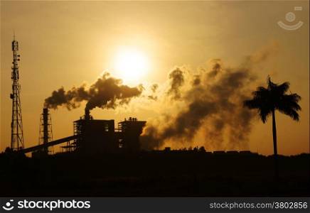 Black smoke from smoke stack of factory in industrial zone rose in to the air, it make polluted enviroment, the plant and tree in silhouette at sunrise, atmosphere cover with waste exhaust