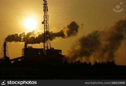 Black smoke from smoke stack of factory in industrial zone rose in to the air, it make polluted enviroment, the plant in silhouette at sunrise, atmosphere cover with waste exhaust
