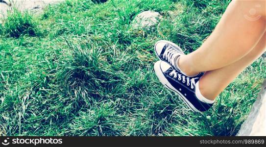 Black sneakers and green grass in the summer: free time for teenager