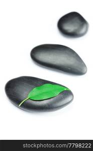black spa stones with green leaf and a drop of water isolated on white
