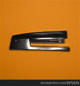 Black stapler on orange background.