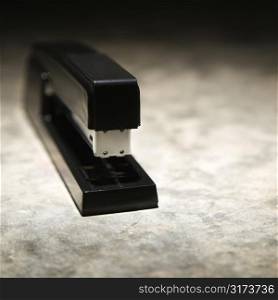 Black stapler on textured background.