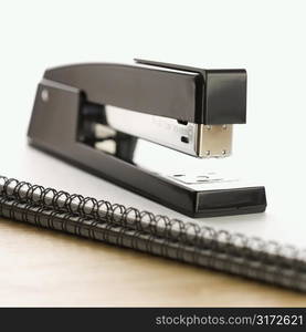 Black stapler on top of a spiral bound notebook.