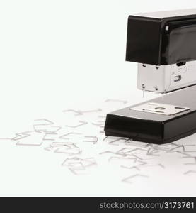 Black stapler on white background surrounded by individual staples.