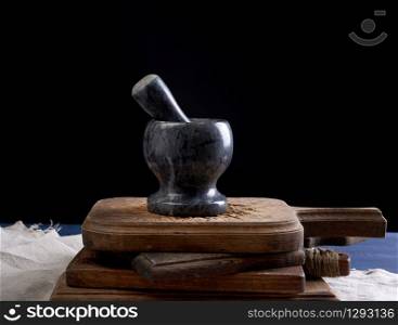 black stone mortar with pestle for grinding spices and herbs on a brown wooden board, black background