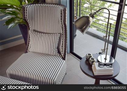 black striped easy chair in the corner with decorative brass lamp and books on wooden round table