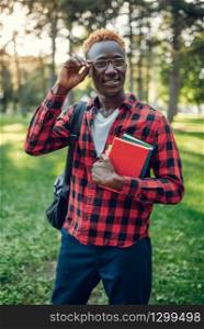 Black student in glasses holds book in summer park. A teenager studying on the grass outdoor. Black student in glasses holds book, summer park
