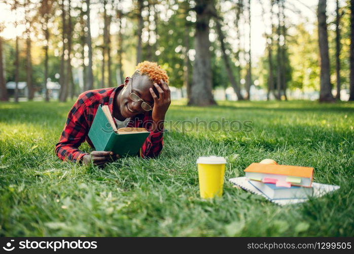 Black student with backpack sitting on the grass in summer park. A teenager studying outdoors and having lunch. Black student with backpack sitting on the grass