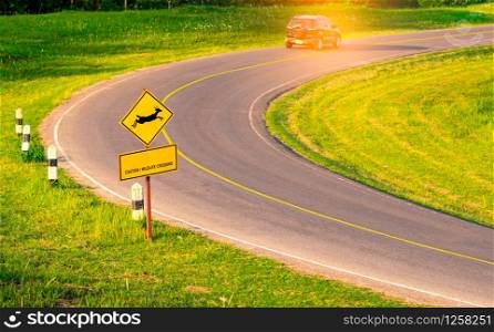 "Black SUV car of the tourist driving with caution during travel at curve asphalt road near yellow traffic sign with deer jumping inside the sign and have message "caution wildlife crossing""