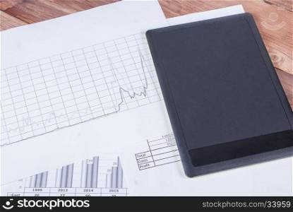 Black tablet on the table on top of financial charts. Black tablet lies in the financial document - tables and graphs