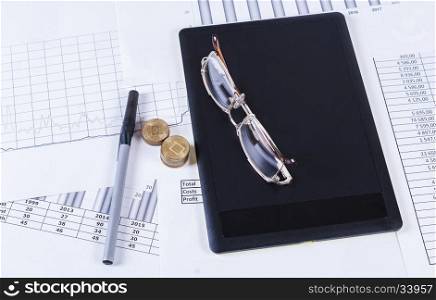 Black tablet ruchkaa and glasses lying on the financial tables and graphs. Financial accounting sales forecast graphs analysis