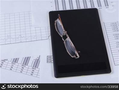 Black tablet with glasses lying on it in the financial tables and graphs. Financial accounting sales forecast graphs analysis