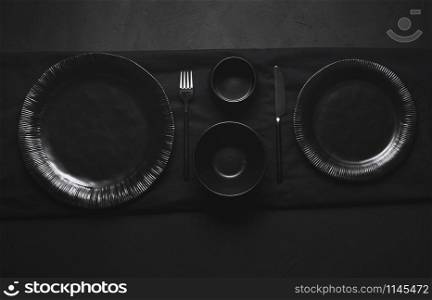 Black tableware, plates, bowls and cutlery, empty dishes, on black table. Flat lay of empty dishes. All black tableware. Dinner settings. Empty plates