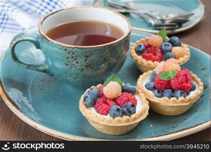 Black tea in a blue vintage cup and fruit tartlets with raspberries and blueberries