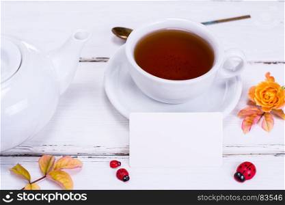 black tea in a round white cup with saucer and brewer, ahead of an empty white paper square business card