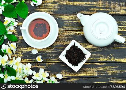 Black tea in a round white cup with saucer and white tea pot on a wooden background, top view