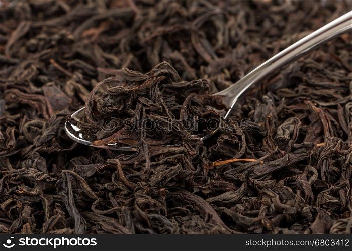 Black tea in a spoon on a black tea background. Close-up shot