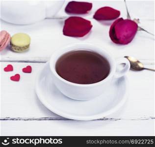 black tea in a white mug with a saucer on a white wooden background