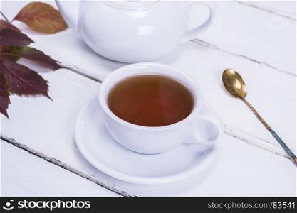 black tea in a white round cup and saucer on a white wooden background, close up