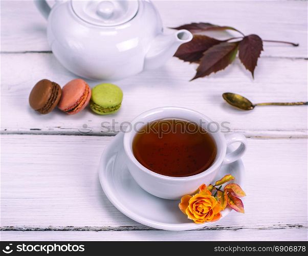 black tea in a white round cup with a saucer on a white wooden background with cakes macarons