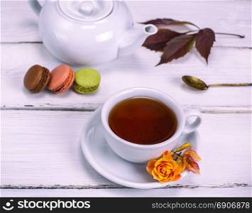 black tea in a white round cup with a saucer on a white wooden background with cakes macarons