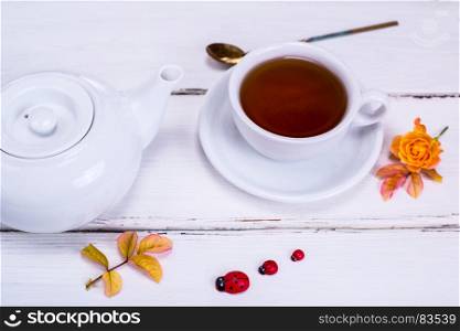 black tea in a white round cup with a saucer on a white wooden background and a white tea pot