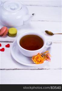black tea in a white round cup with a saucer on a white wooden background, behind a white tea pot