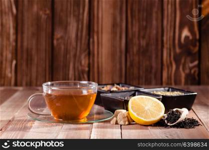 Black tea with lemon and brown sugar cubes on the wooden table, place for text. Various types of tea