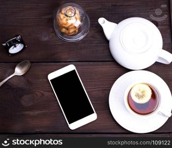 black tea with lemon in a round white ceramic cup with a saucer on a brown wooden background