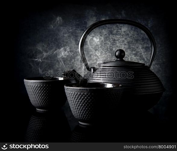 Black teapot with small cups on black background