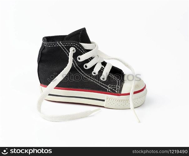 black textile children&rsquo;s sneaker with white untied shoelaces on a white background, shoes stand sideways