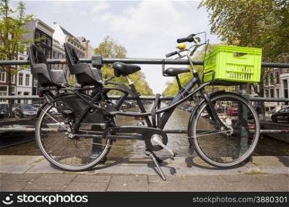 black transport bicycle for children and groceries on bridge over canal in amsterdam