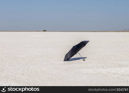 Black umbrella lies on cracked drought salt lake located in Central Anatolia with clean blue sky.Aksaray,Turkey.Copy space for editing.. Black umbrella lies on cracked drought salt lake