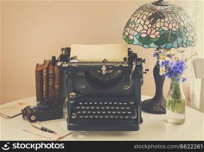 black vintage typewriter with books on wooden table with art nuveau l&, retro toned. typewriter on table