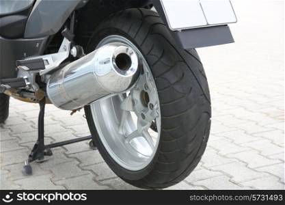 Black wheel of a motorcycle with the chromeplated muffler the rear view