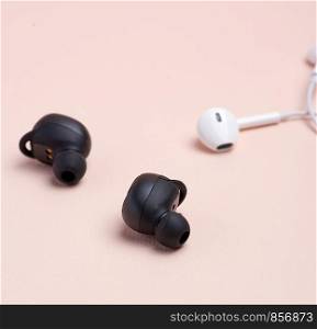 black wireless and white earphones with wire on a beige background, technology concept