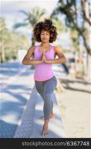 Black woman, afro hairstyle, doing yoga in the beach. Young Female wearing sport clothes.