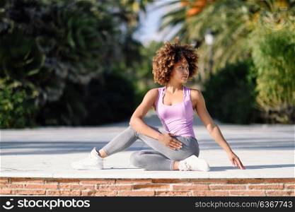Black woman, afro hairstyle, doing yoga on promenade. Young Female wearing sport clothes