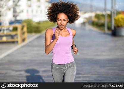 Black woman, afro hairstyle, running outdoors in urban road. . Black woman, afro hairstyle, running outdoors in urban road. Young female exercising in sport clothes.
