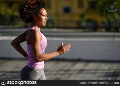 Black woman, afro hairstyle, running outdoors in urban road. Young female exercising in sport clothes.