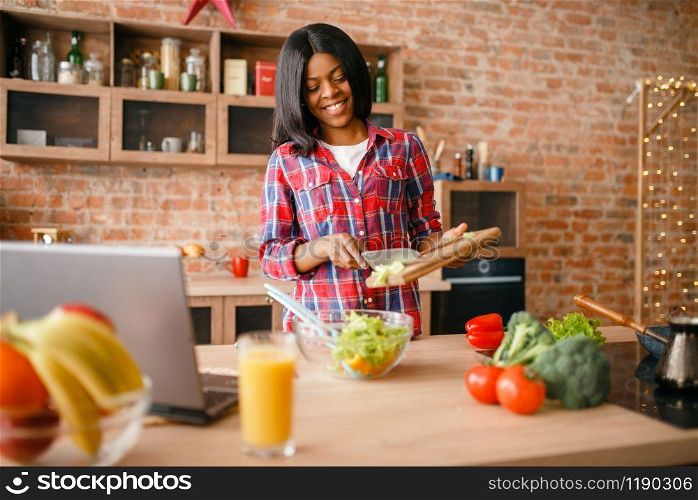 Black woman cooking breakfast on the kitchen. African female person preparing vegetable salad at home. Healthy vegetarian lifestyle. Black woman cooking salad on the kitchen