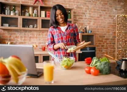 Black woman cooking breakfast on the kitchen. African female person preparing vegetable salad at home. Healthy vegetarian lifestyle. Black woman cooking salad on the kitchen