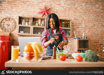 Black woman in apron cooking healthy breakfast on the kitchen. African female person preparing vegetable salad at home. Black woman in apron cooking healthy breakfast