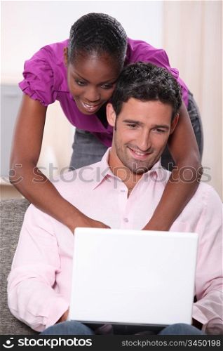 black woman leaning on his boyfriend and doing computer laid on his boyfriend&rsquo;s knees