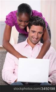 black woman leaning on his boyfriend and doing computer laid on his boyfriend&rsquo;s knees