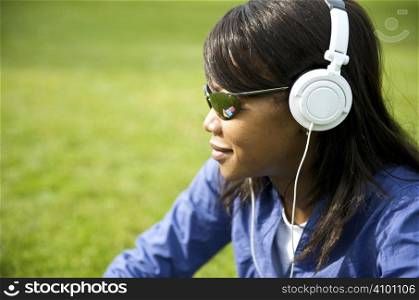 Black woman listening to the music in a park with white headphones