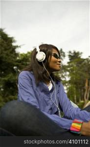 Black woman listening to the music in a park with white headphones