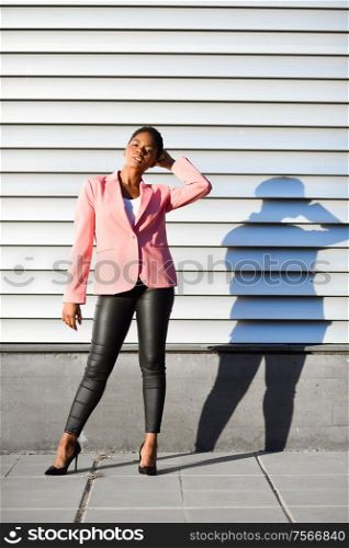 Black woman, model of fashion, standing on urban wall. African american female wearing suit with pink jacket with sunset light.. Black woman, model of fashion, standing on urban wall