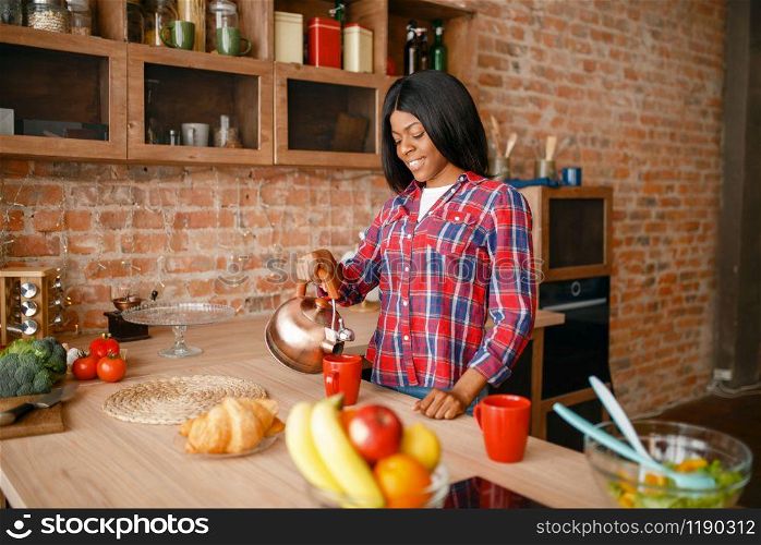 Black woman prepares coffee on breakfast on the kitchen. African female person preparing vegetable salad at home
