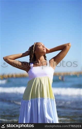 Black woman walking along the shore of the beach wearing a beautiful long dress. Young girl enjoying her vacations.. Black woman walking along the shore of the beach wearing a beautiful long dress.